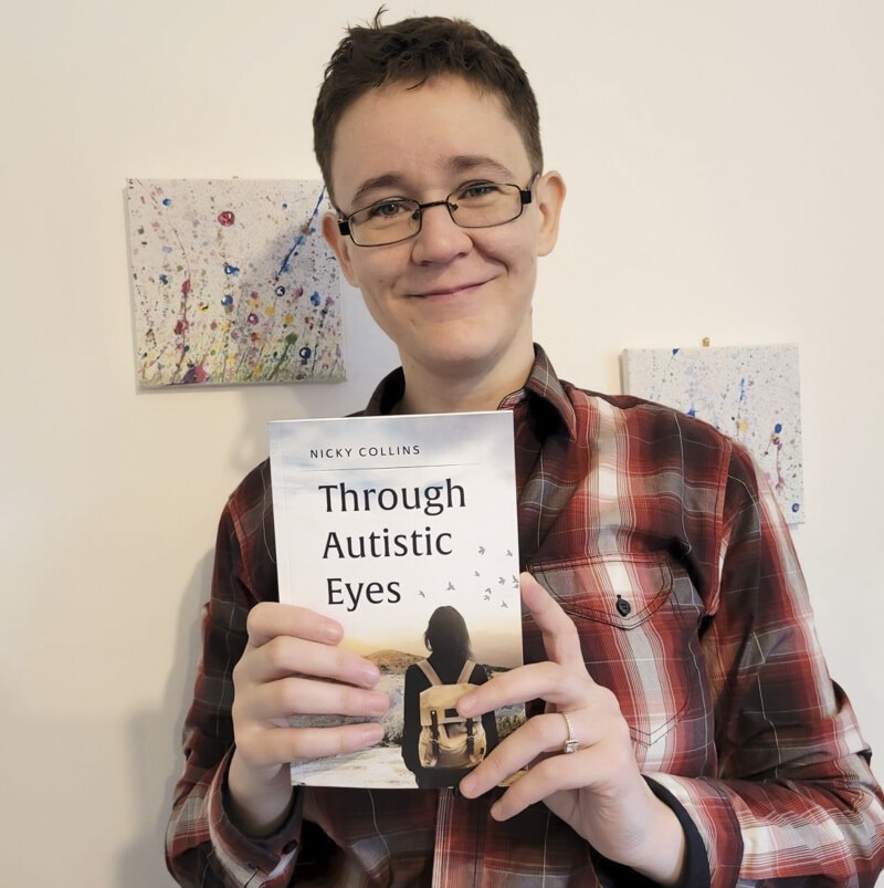 Photograph of the author Nicky Collins holding her book Through Autistic Eyes